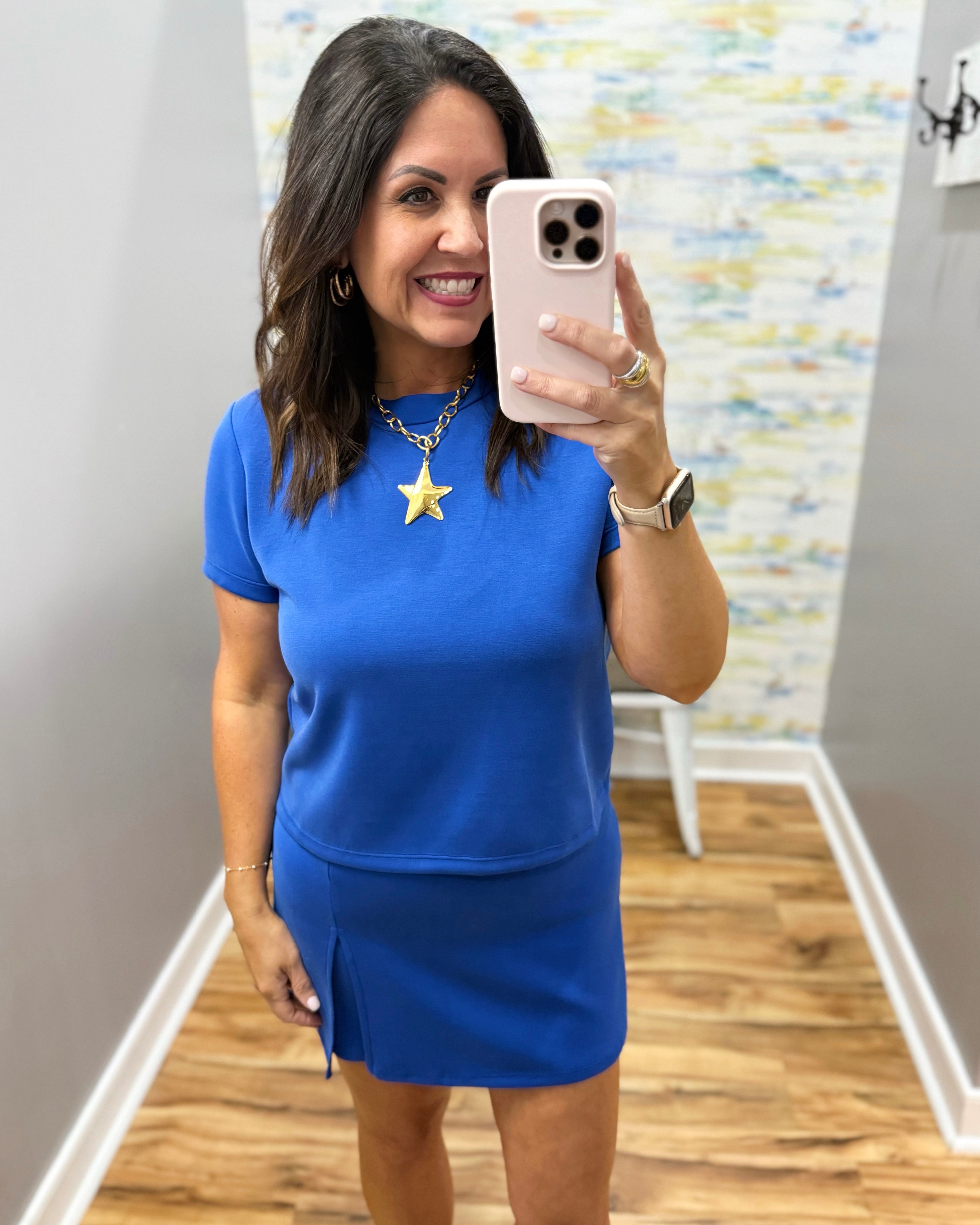 Woman taking a mirror selfie wearing a blue outfit with a star necklace.