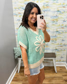 Woman taking a mirror selfie wearing a green and beige patterned sweater.