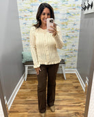 A woman takes a mirror selfie in a fitting room wearing a cream cable-knit button-front cardigan and dark brown wide-leg pants.