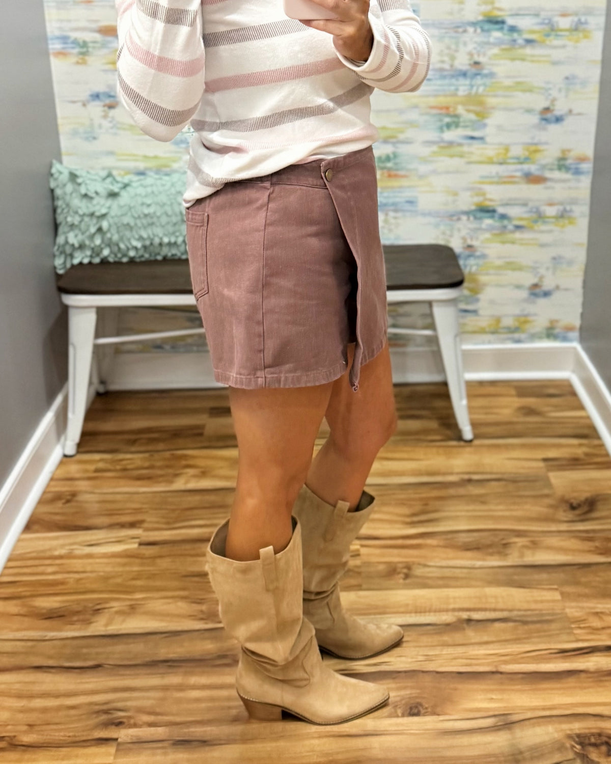 A person wearing a chestnut color wrap-style mini skirt with a single button closure, paired with a pink and white striped long-sleeve top and Corkys City Slicker boots in Sand Faux Suede.