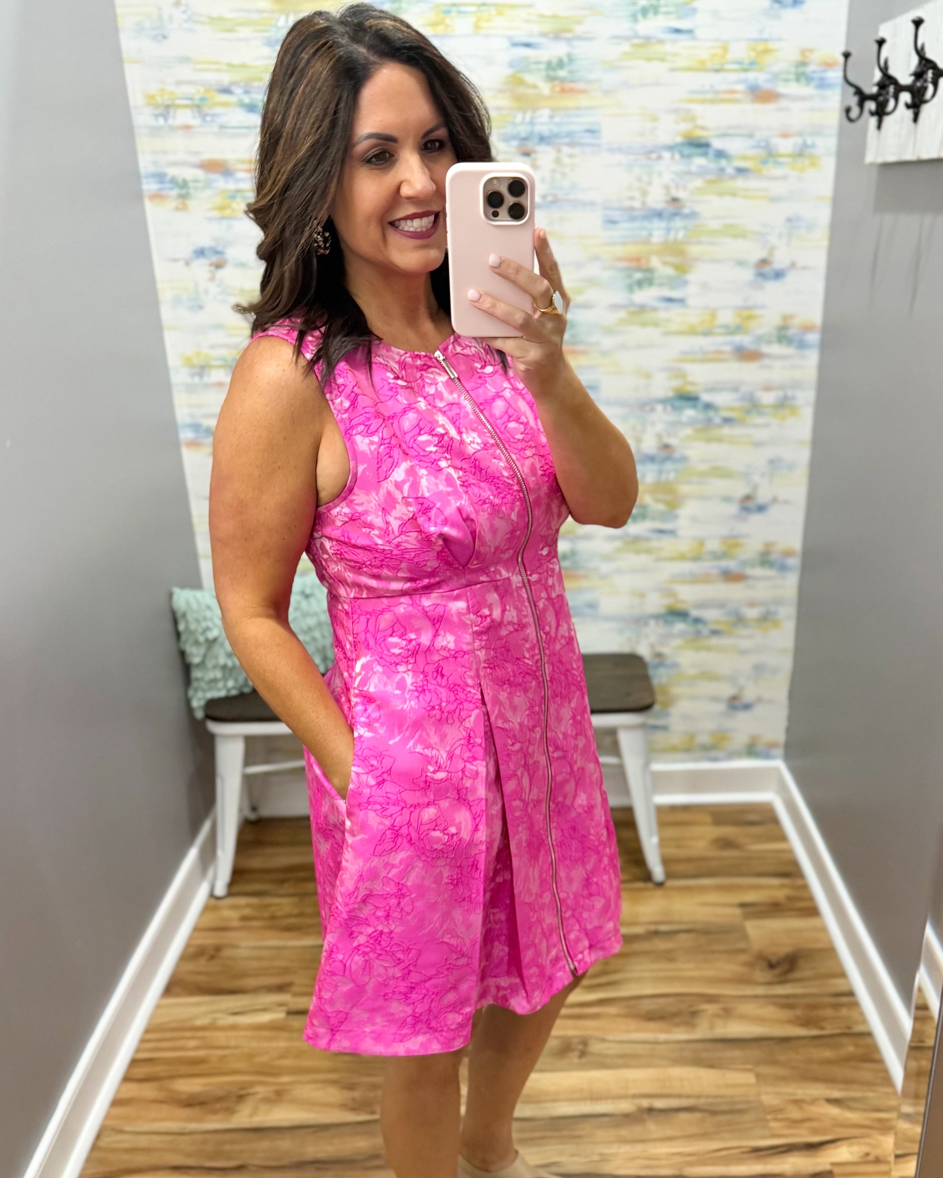 Woman taking a mirror selfie wearing a pink dress in a room with a colorful wall.