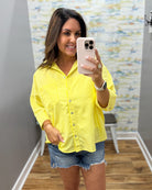 Woman taking a mirror selfie wearing a yellow striped shirt and denim shorts.