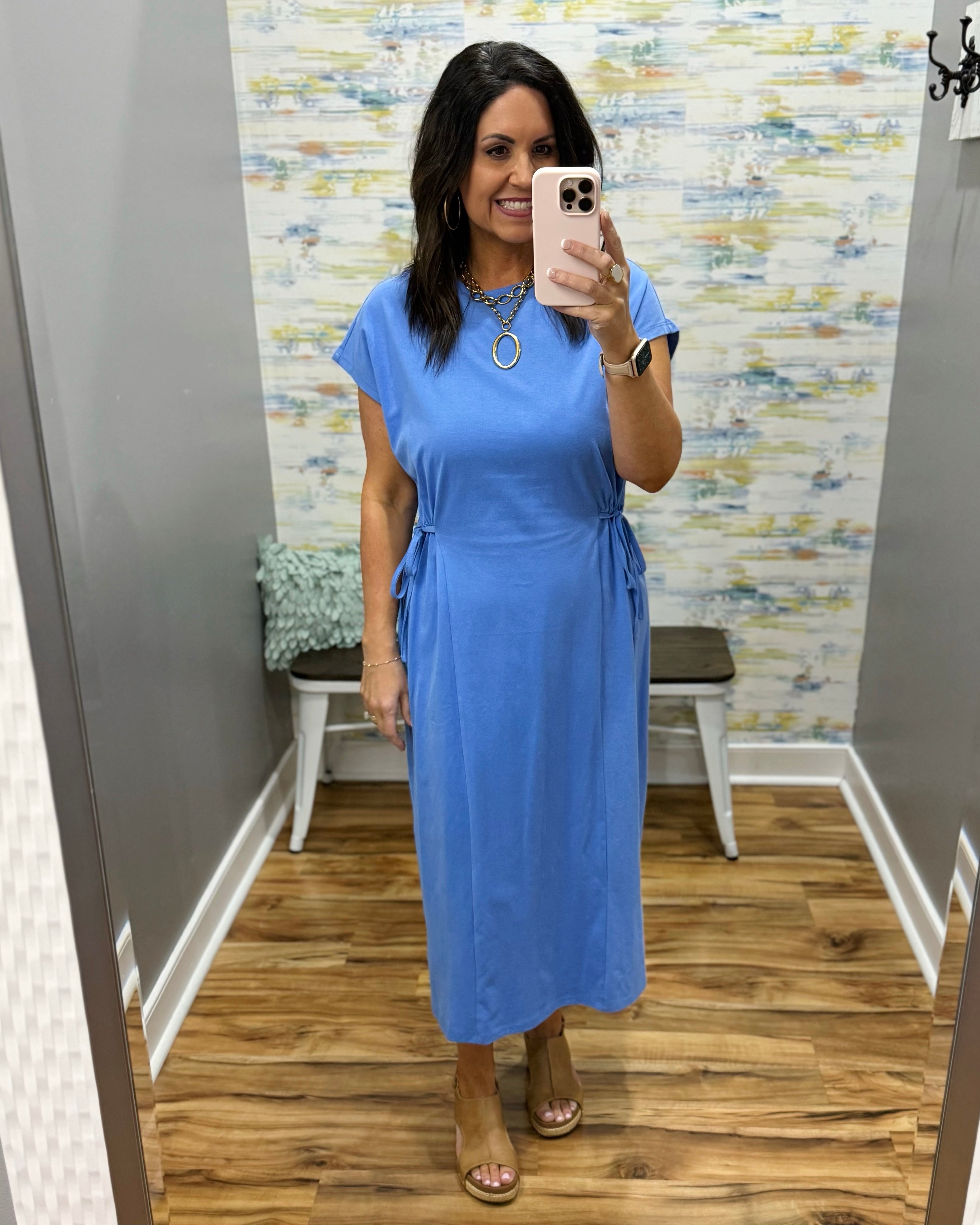 Woman wearing a blue dress in a room with patterned wallpaper.