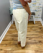 Person wearing cream-colored pants standing on a wooden floor.