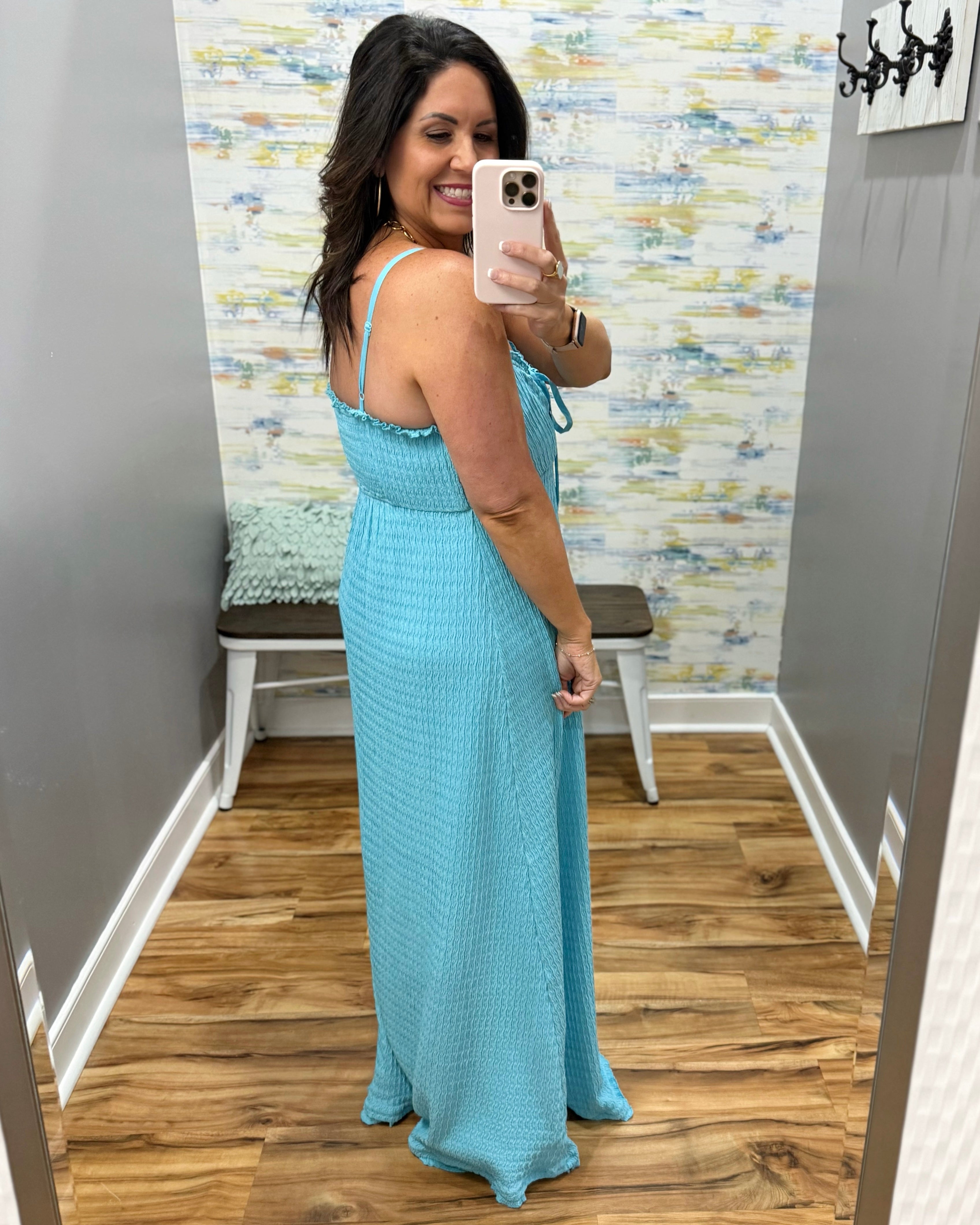 Woman taking a mirror selfie wearing a light blue dress in a room with patterned wallpaper.