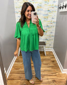 Woman taking a mirror selfie wearing a green top and blue jeans in a store.