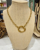 Chansuttpearls Scottie chunky gold chain necklace with a large textured circular ring pendant, displayed on a beige fabric-covered jewelry bust in a retail store setting.