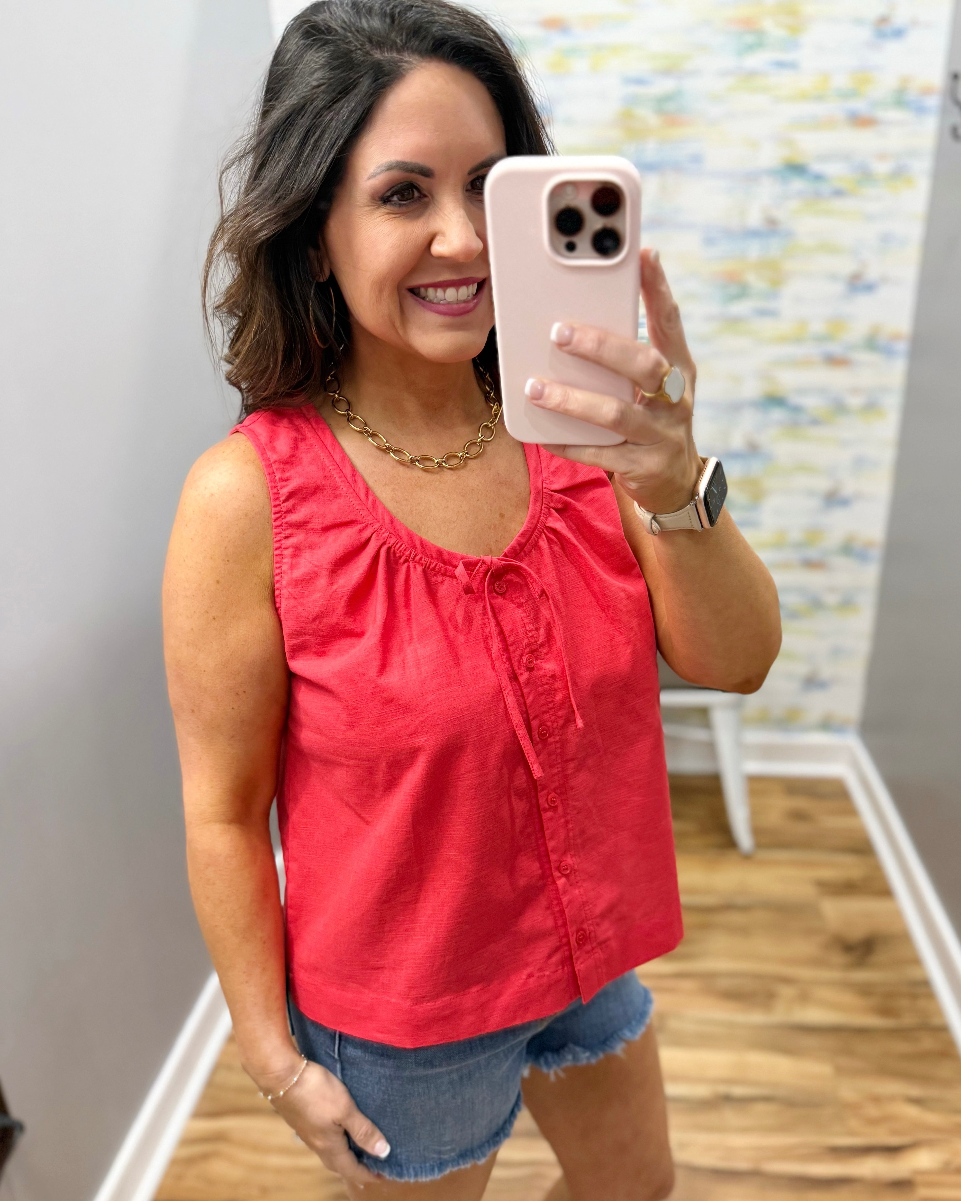 Woman wearing a red sleeveless top and denim shorts.