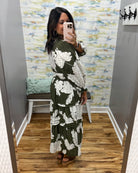 A woman takes a mirror selfie wearing a long-sleeve olive green maxi dress with a white floral print. The dress features a V-neckline, smock waist.