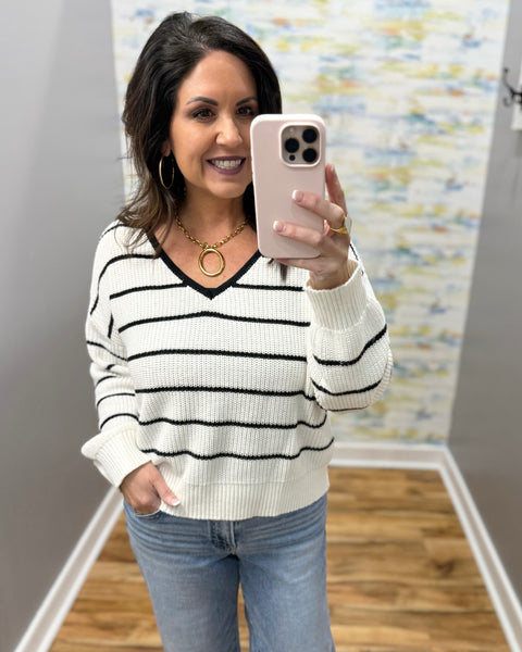 Woman taking a mirror selfie wearing a black and white striped sweater and blue jeans.