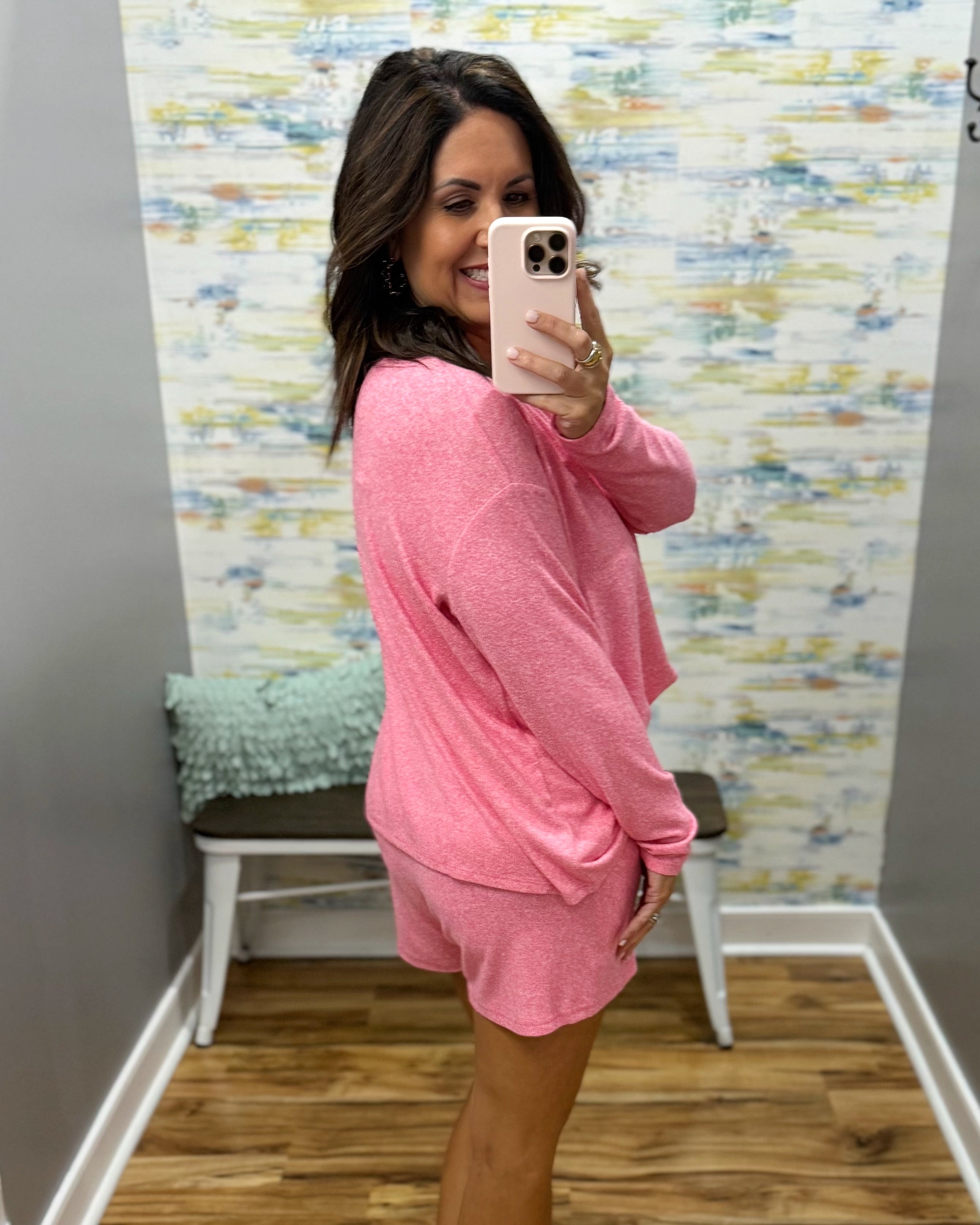 Woman wearing a pink outfit taking a mirror selfie in a room with colorful wall art.
