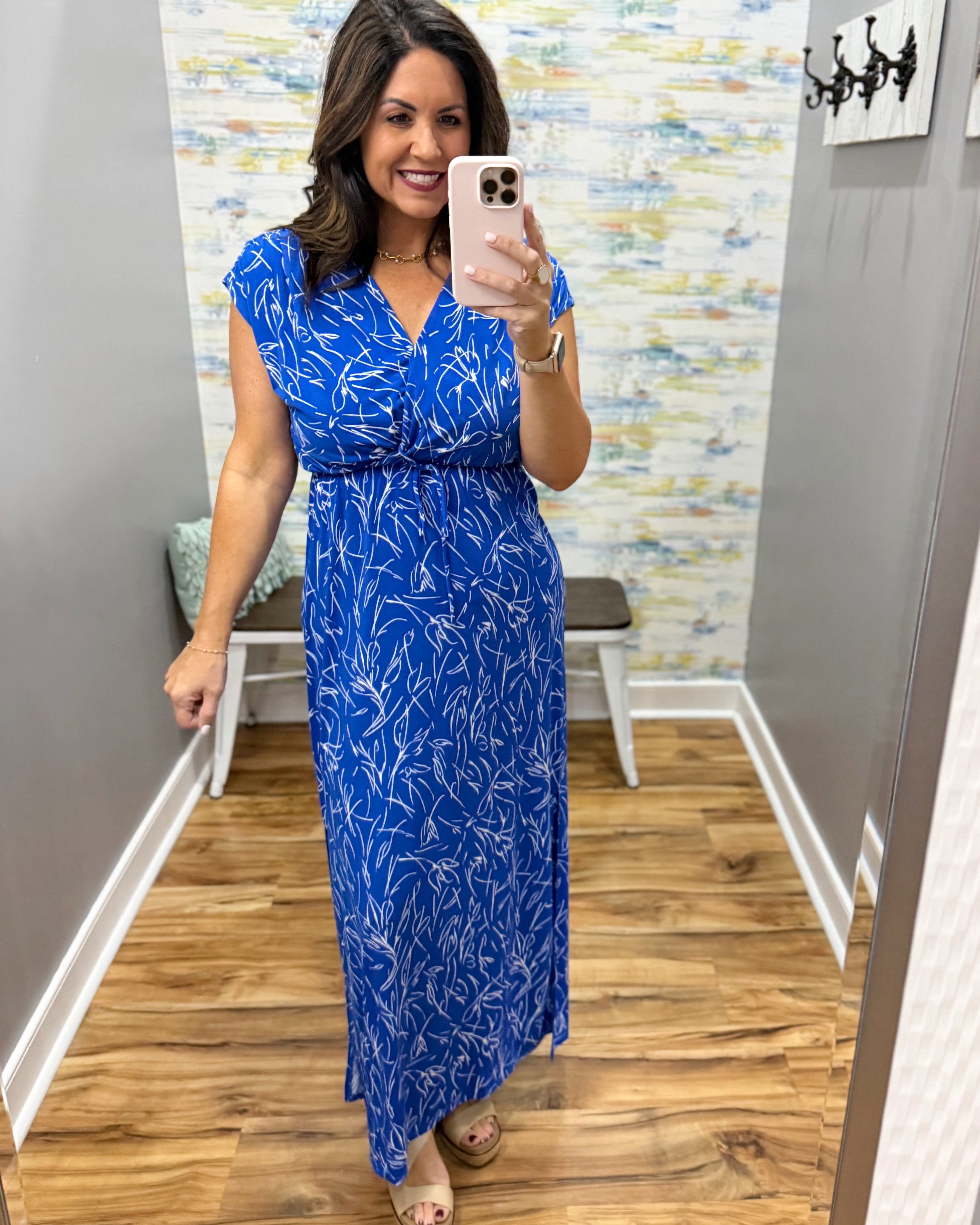 Woman taking a mirror selfie wearing a blue dress with a floral pattern in a room with a textured wall.