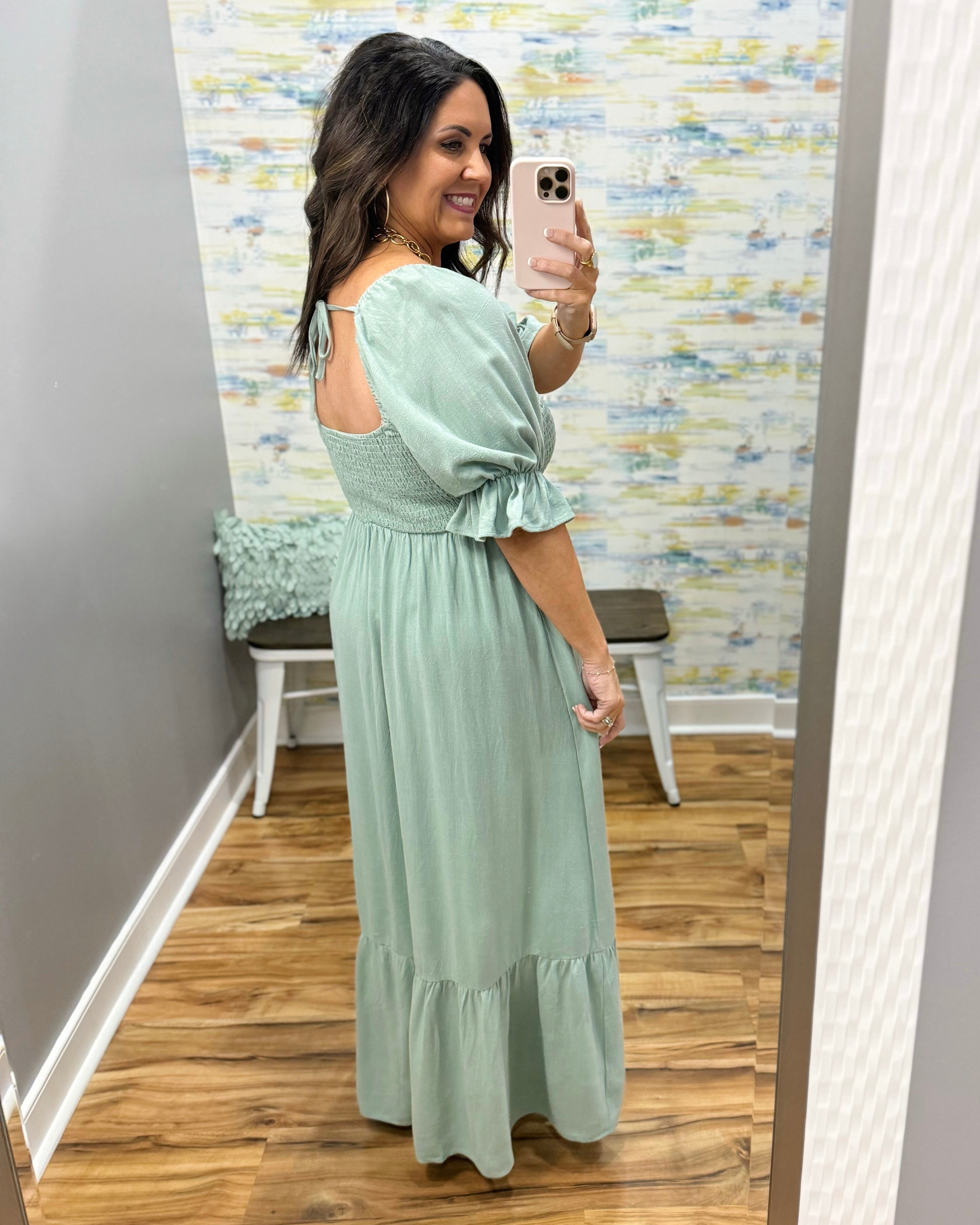 Woman wearing a light green dress with ruffled sleeves and bottom, standing in front of a mirror.