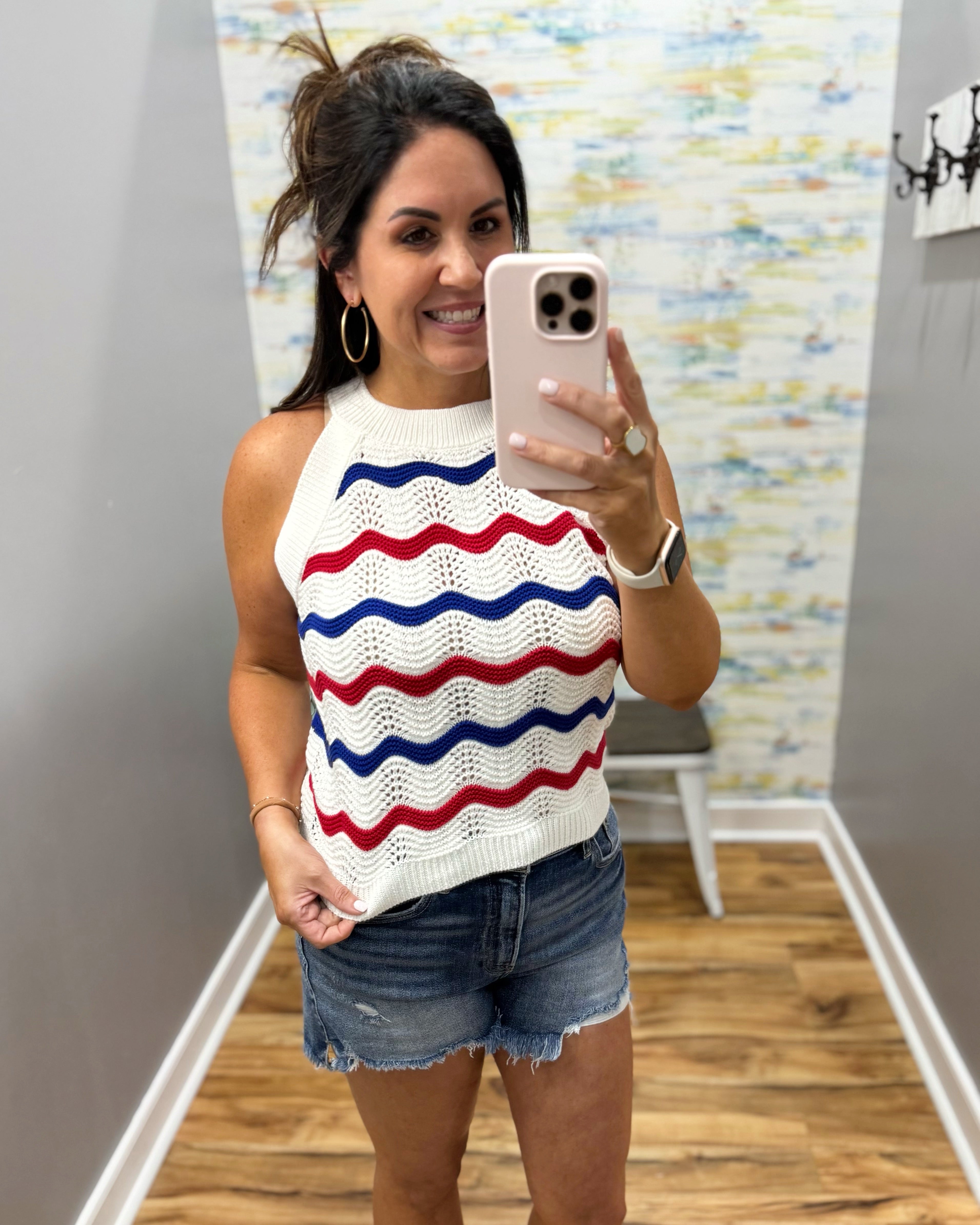 Woman taking a mirror selfie wearing a sleeveless sweater with red and blue stripes.