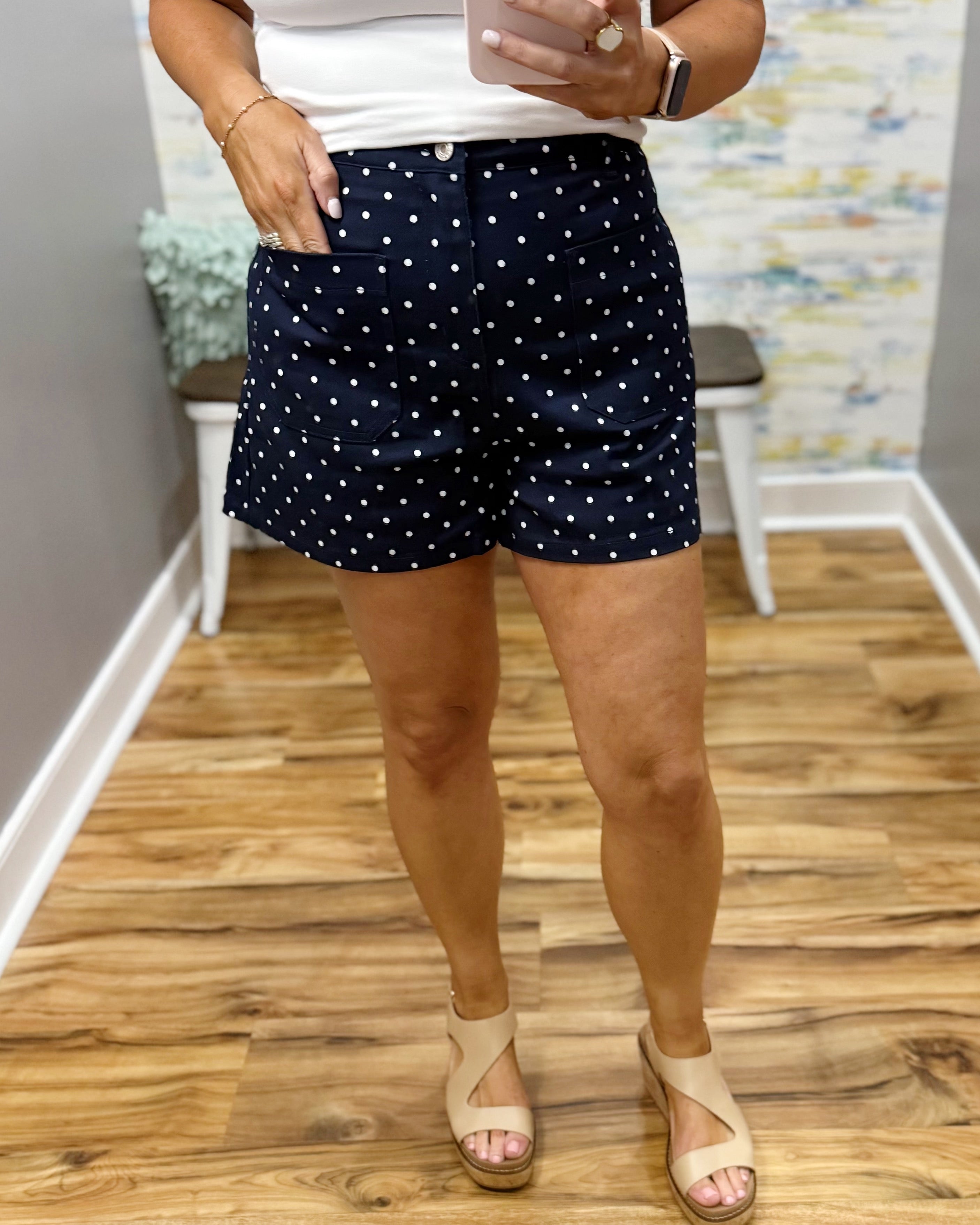 Person wearing navy shorts with white polka dots indoors on a wooden floor.