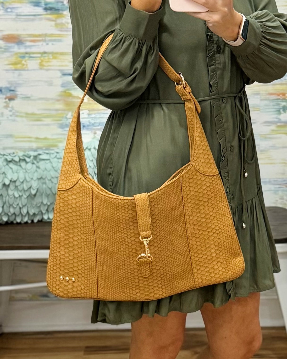 A woman wearing an olive green dress carries a large mustard yellow textured shoulder bag with a gold-tone clasp and strap.