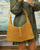 A woman wearing an olive green dress carries a large mustard yellow textured shoulder bag with a gold-tone clasp and strap.
