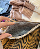 A close-up of a beige Gucci zip pouch with a gold zipper, held open by a hand. The interior features the signature Gucci GG monogram pattern in black.