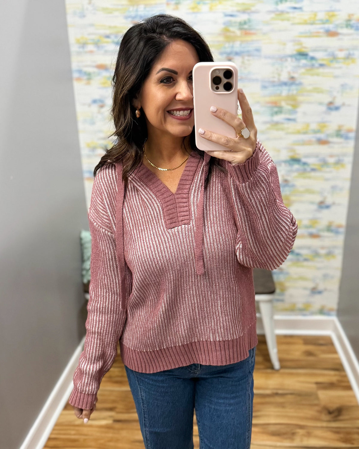 A woman takes a mirror selfie wearing a ribbed long-sleeve V-neck pullover sweater in a dusty rose pink color, paired with blue jeans.
