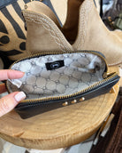 A close-up of a black leather zip pouch with gold-tone hardware, held open by a hand. The interior is lined with a light gray patterned fabric featuring the 'pup' brand logo.