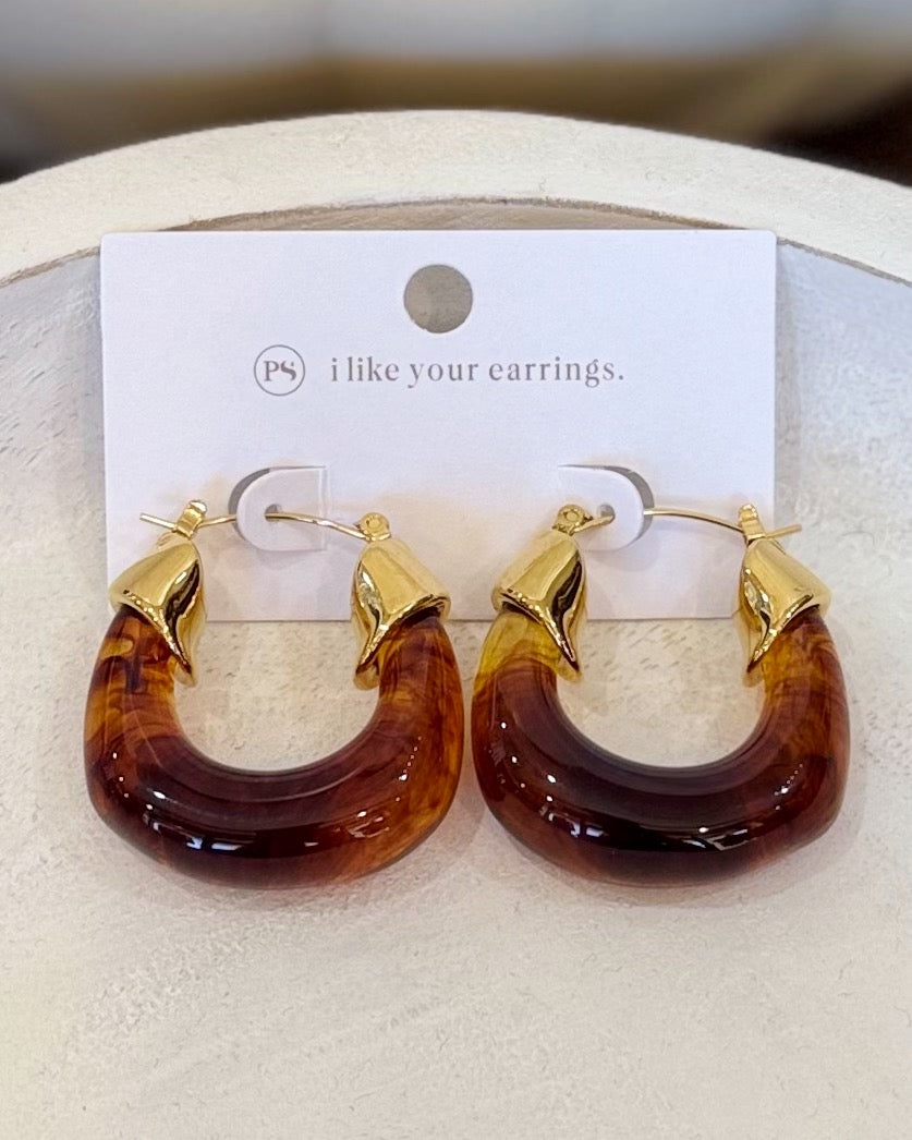 A pair of gold hoop earrings with amber-brown marbled resin or horn-like curved drops, displayed on a white card that reads 'i like your earrings.' against a soft beige background.